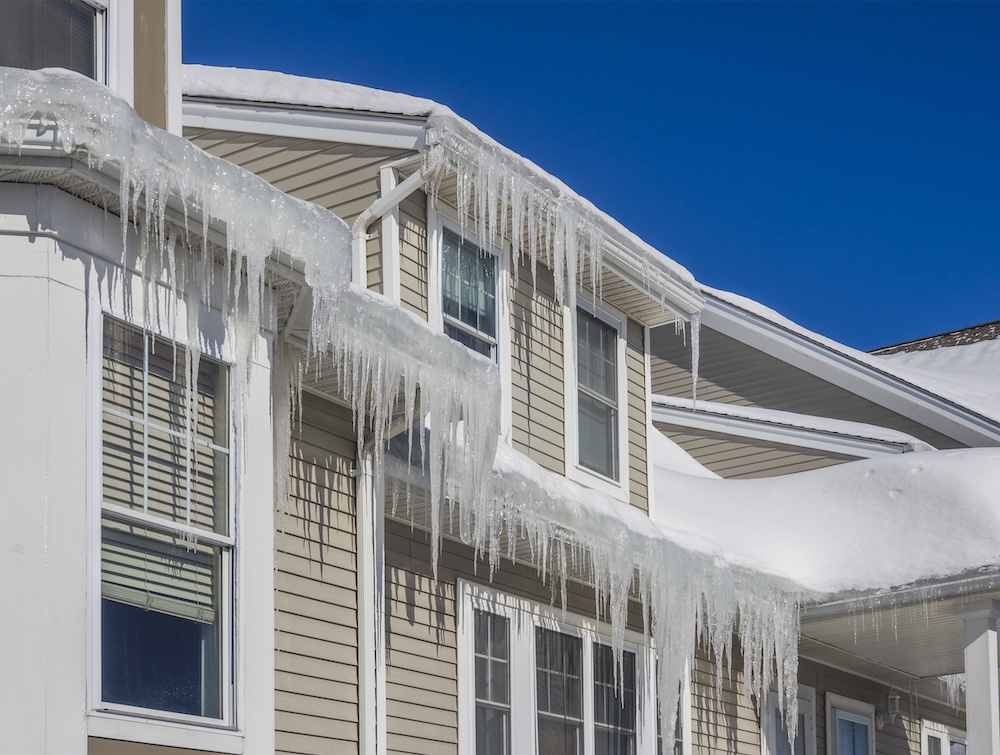 Home with heavy ice dams and large icicles on a clear winter day